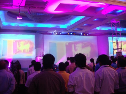 The keynote audience at TechEd Sri Lanka standing in a dimly lit hall, facing large screens that show the Sri Lankan flag
